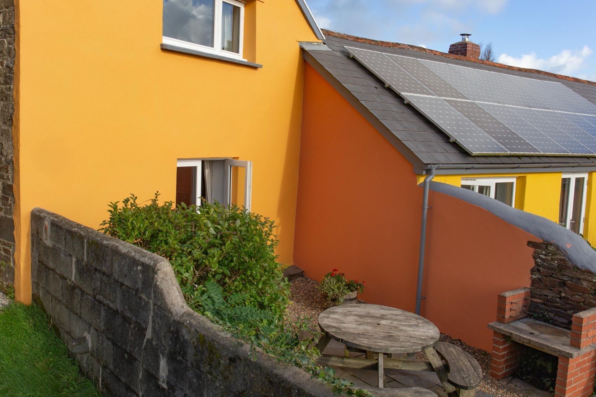 Una casa gialla con tetto solare, una piccola finestra e un muro in pietra.