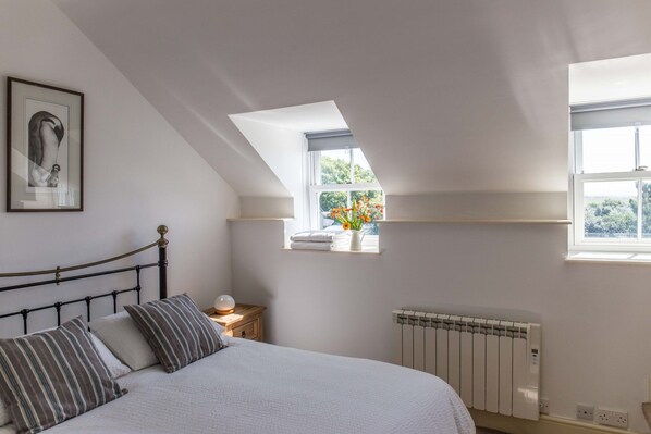 A bedroom with a bed, a nightstand, a radiator, and a window with a view of greenery.