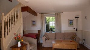 A living room with a staircase, a sofa set, a wooden coffee table, and a vase with flowers. - The Dairy, shared hot tub and sauna (Hartland)