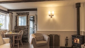 A cozy living room with a stone wall, a fireplace, a dining area with a table and chairs, and a sofa. - The Linhay, shared hot tub and sauna (Hartland)