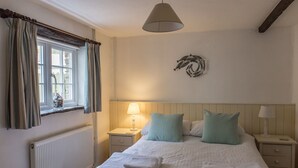 A bedroom with a bed, two bedside tables, a radiator, and a window with curtains. - The Linhay, shared hot tub and sauna (Hartland)