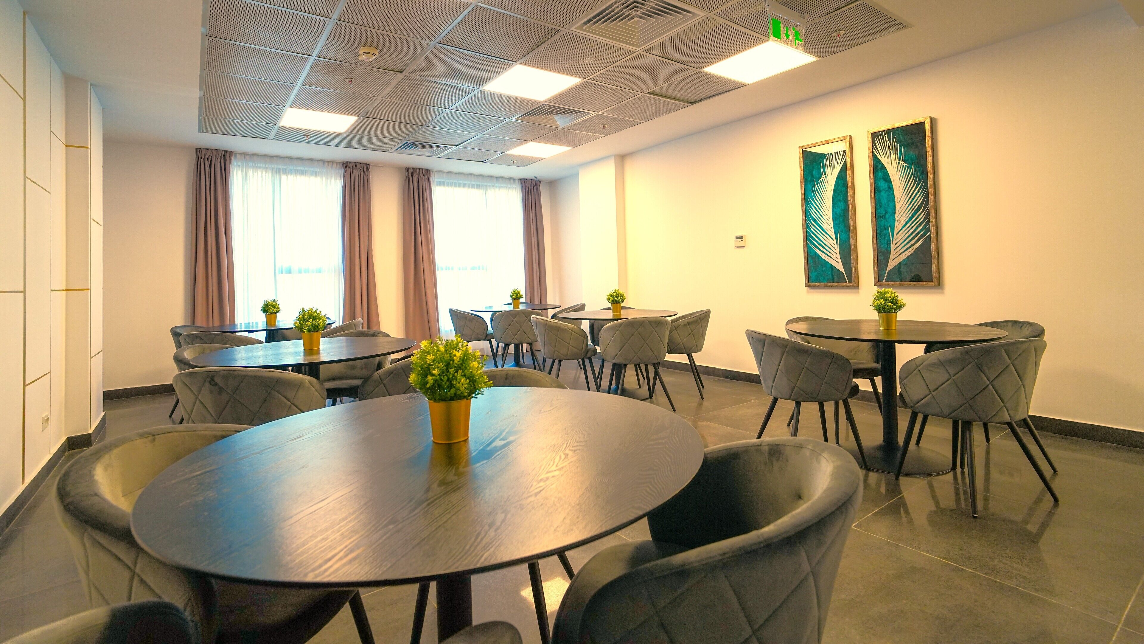A conference room with round tables, grey upholstered chairs, and potted plants.