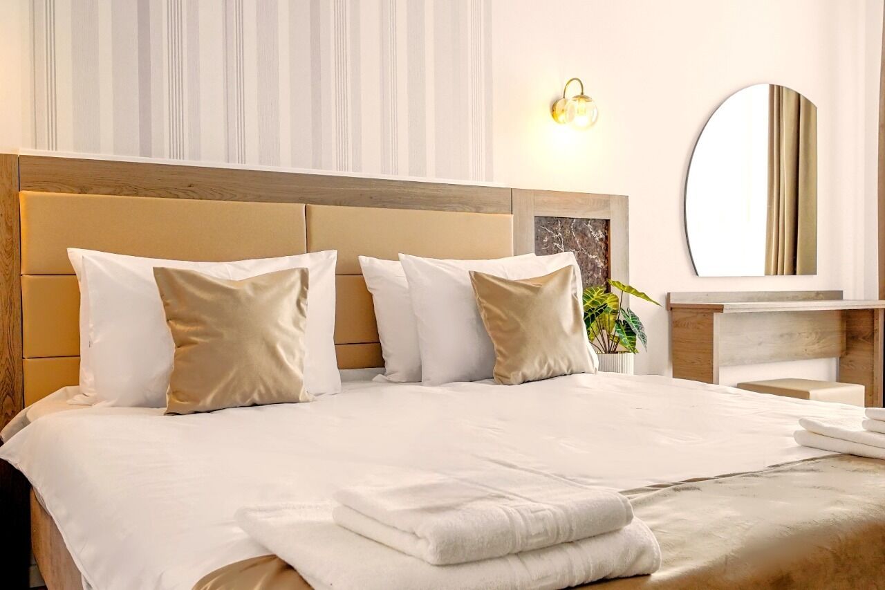 A hotel room with a large bed, a wooden headboard, a bedside table, a mirror, and a plant.
