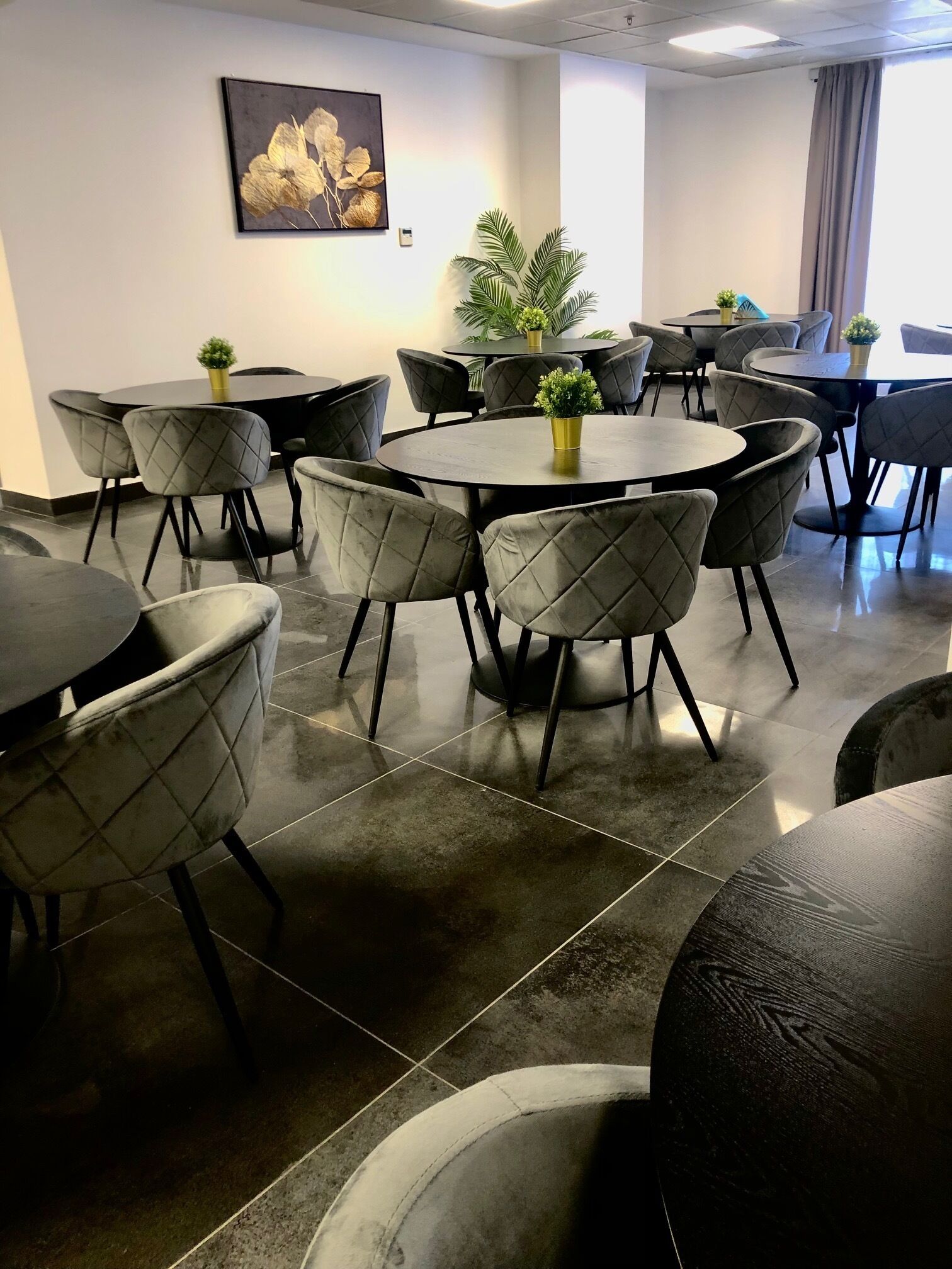Un salón de conferencias con mesas redondas y sillas acolchadas, una planta en maceta y una obra de arte enmarcada en la pared.