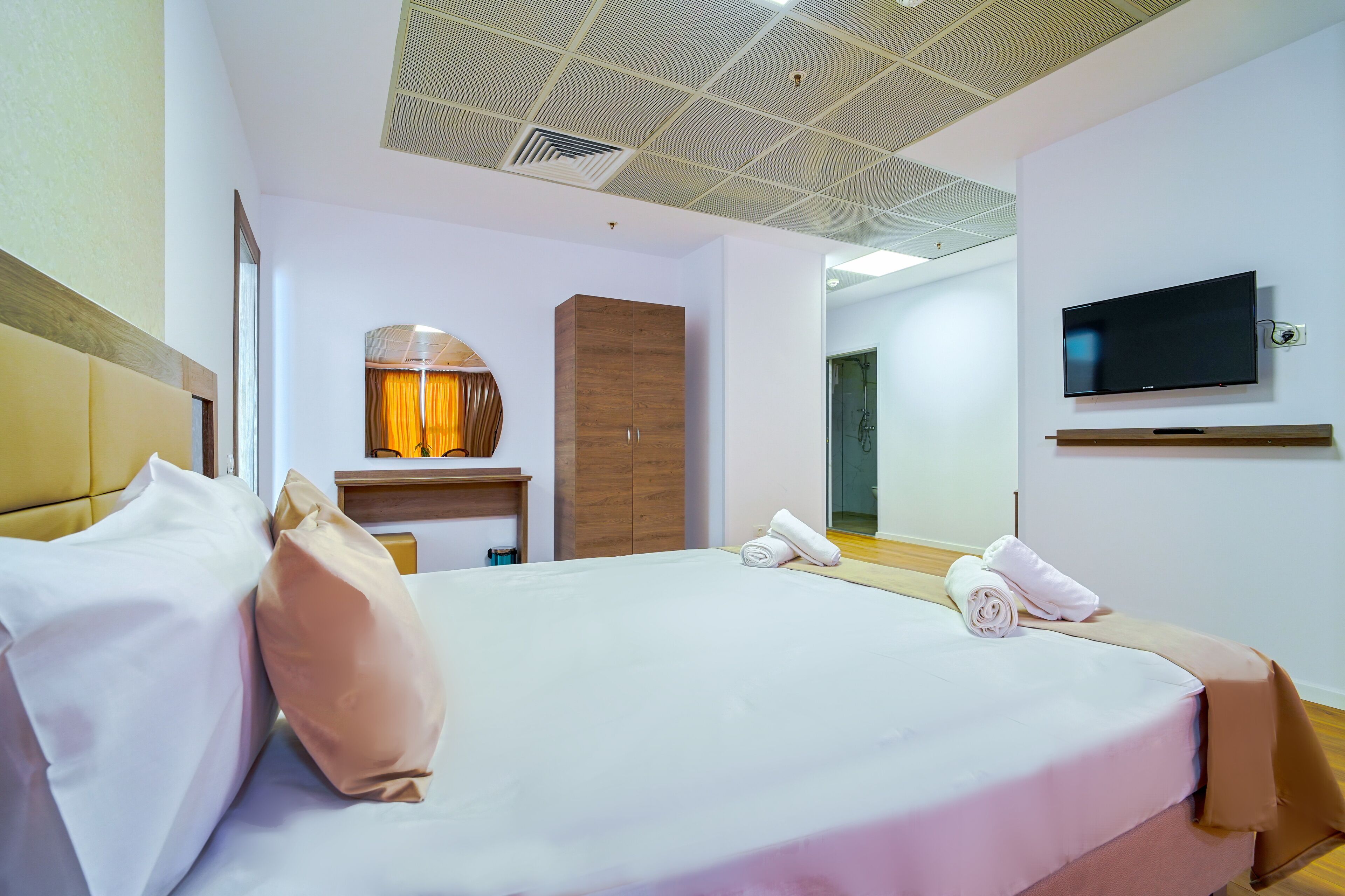 Una habitació d'hotel amb un llit gran, televisió penjada a la paret, un armari i un mirall.