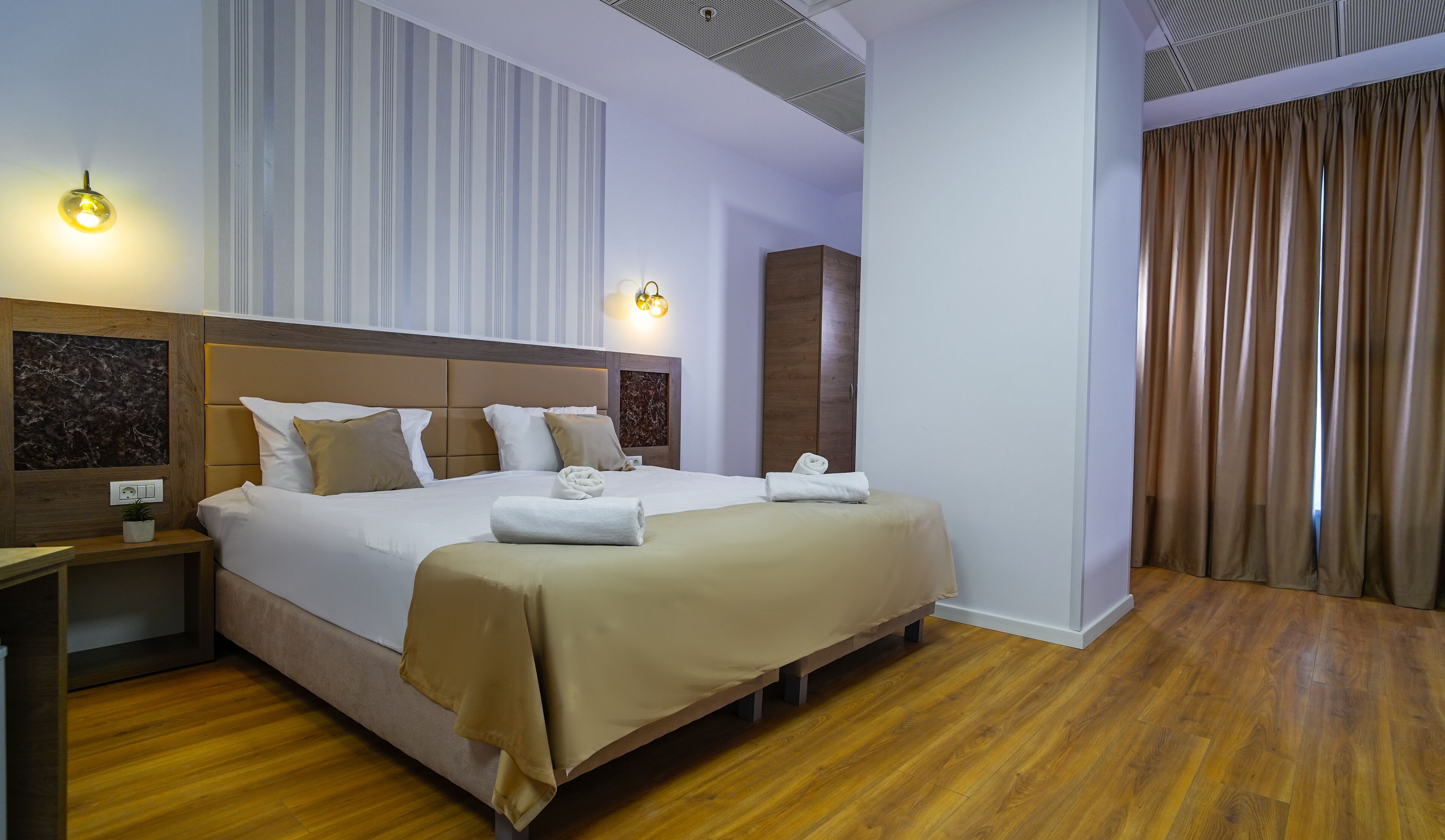 A hotel room with a large bed, bedside tables, a wardrobe, and a bathroom visible through an open door.