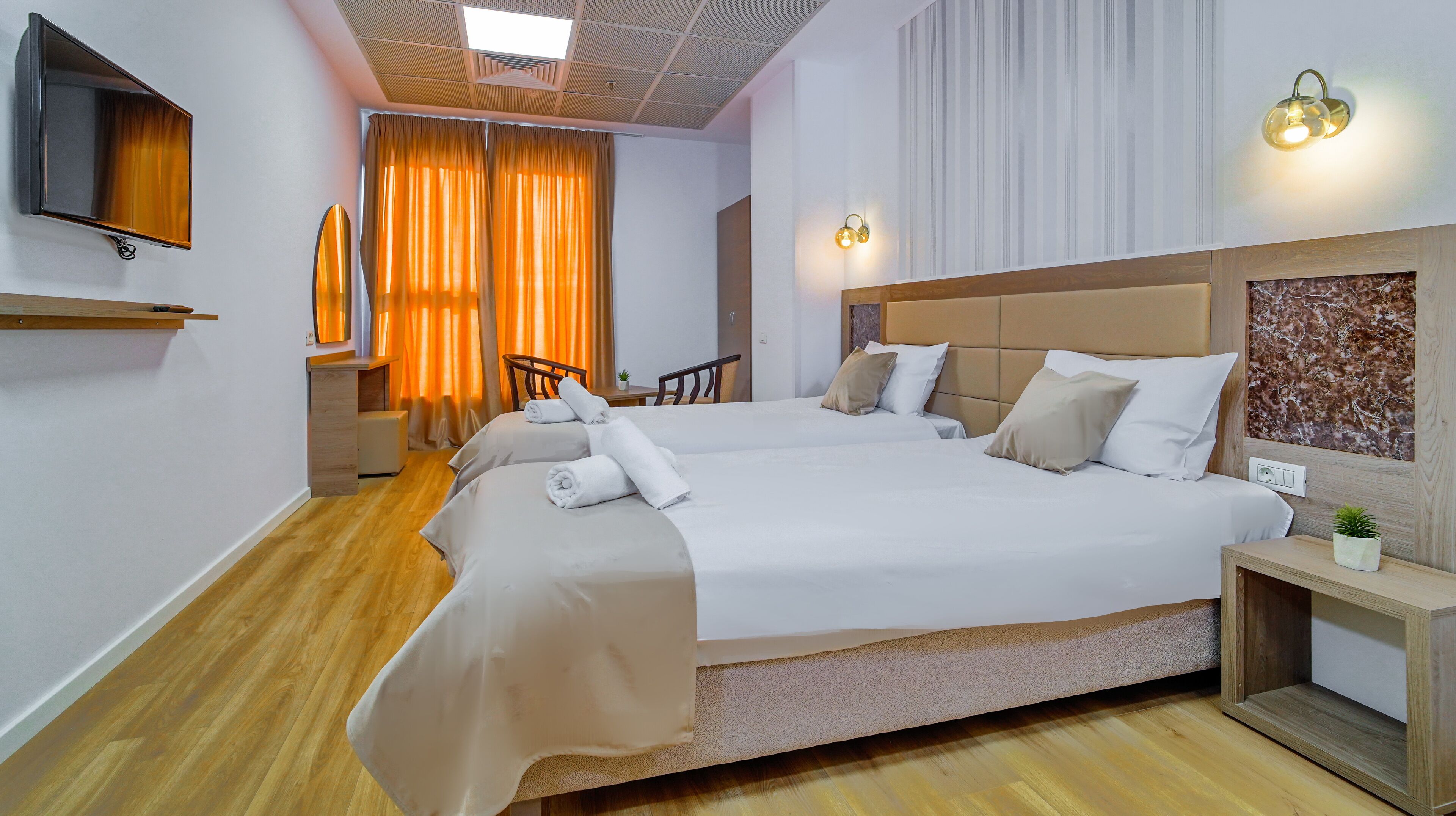 Habitación de hotel con dos camas, un escritorio, una silla, un televisor y una lámpara fijada a la pared.