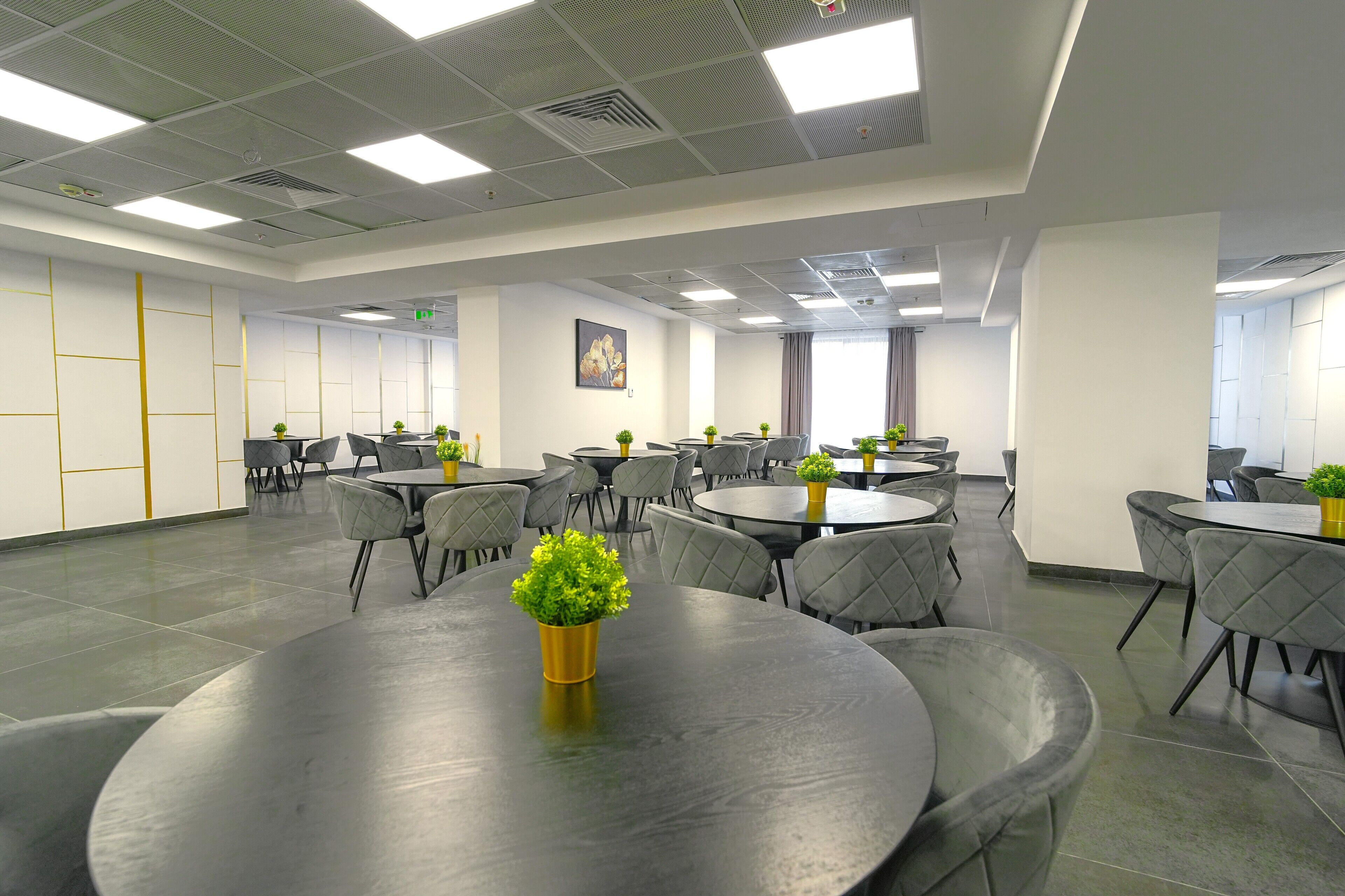 A conference room with multiple tables and chairs, equipped with ceiling lights and potted plants.