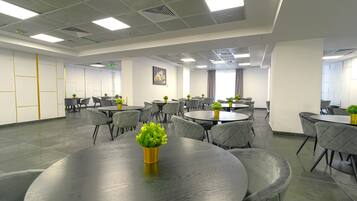A conference room with multiple tables and chairs, equipped with ceiling lights and potted plants.
