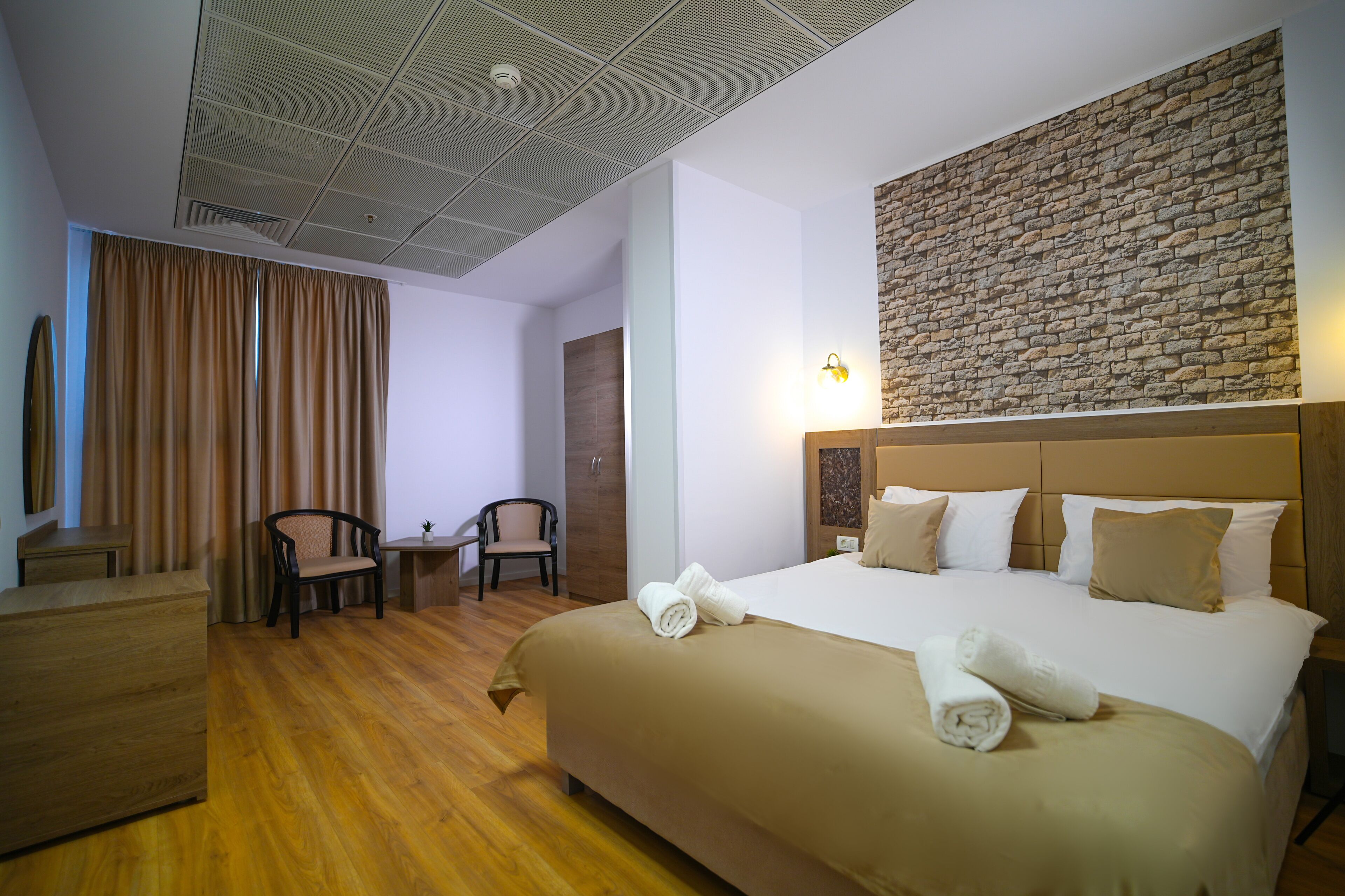 Habitación de hotel con una cama grande, un muro decorativo de ladrillo, un escritorio de madera, una silla y una mesita.
