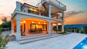A two-story house with a balcony, a pool, and a patio area with seating.