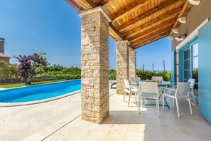 Relax by the pool in this serene outdoor space, featuring a stone column and a dining area with comfortable seating.