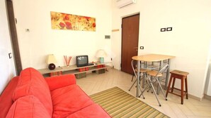 A living room with a red sofa, a small TV, a table with chairs, and a door. - Cornaredo apartment 10 minutes from Milan (Cornaredo)