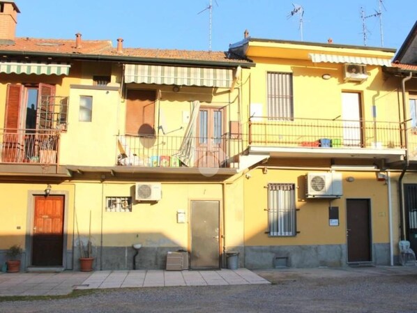 A yellow building with a balcony, a door, and an air conditioning unit. - Cornaredo apartment 10 minutes from Milan (Cornaredo)