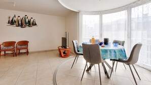 Un coin repas avec une table ronde, des chaises grises, une nappe colorée et une décoration murale représentant un voilier.