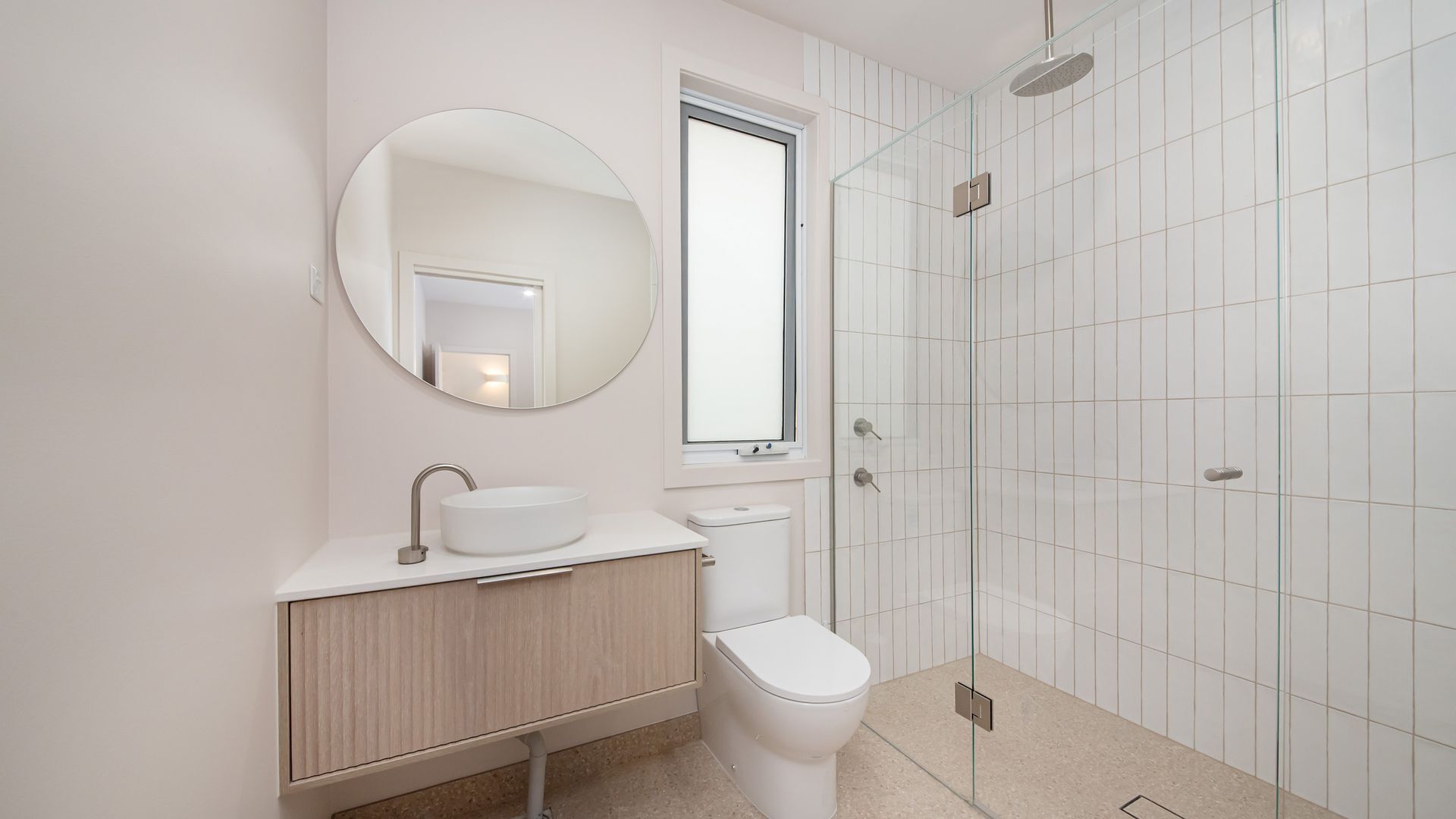 Ein modernes Badezimmer mit rundem Spiegel, Waschbecken in Weiß, Toilette und Duschkabine.