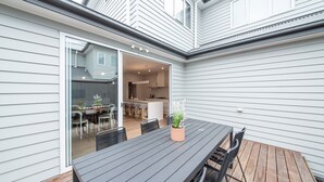 A patio with a table and chairs, a potted plant, and a sliding glass door leading to a kitchen and dining area.