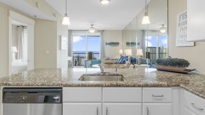 A modern kitchen with granite countertops, a dishwasher, and a dining area with a view. - Beach view condo w/ pool & free attraction tickets (Panama City Beach)