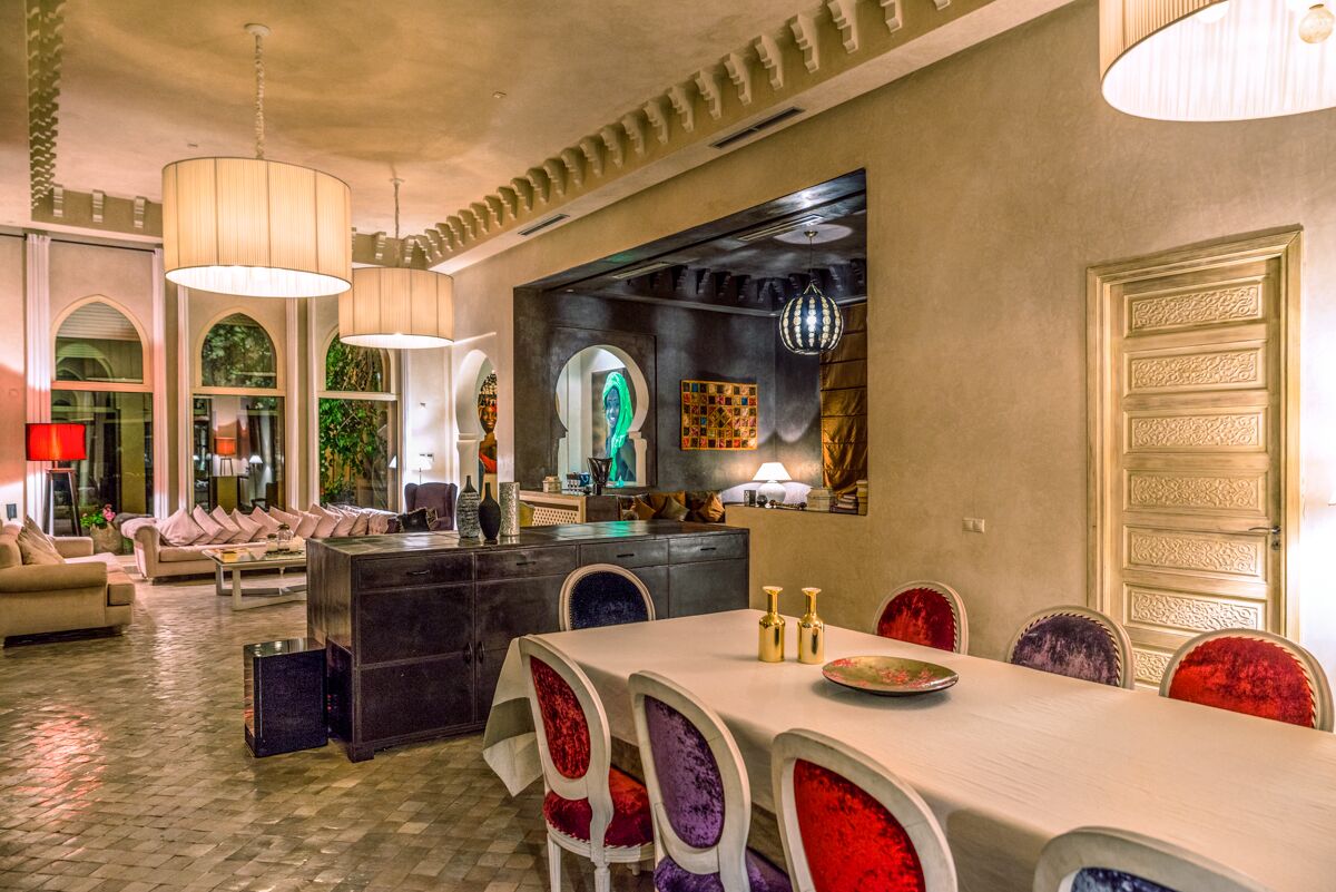 A dining area with a long table, chairs with colorful upholstery, and pendant lighting.