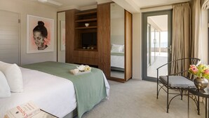 Habitación de hotel con cama, escritorio y silla, estantería y puerta corrediza a un balcón.