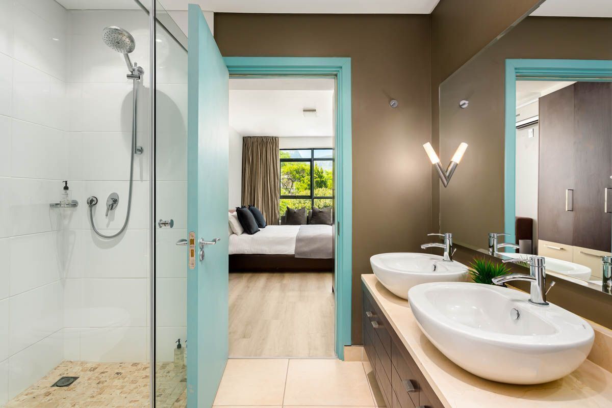 Un baño moderno con ducha de vidrio, dos lavamanos y un espejo grande.