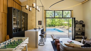 Une cuisine moderne équipée d’un baby-foot, d’un coin bar et offrant une vue sur une piscine.