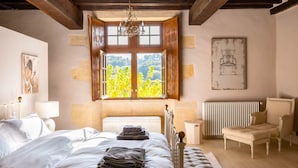 Une chambre avec un grand lit, une fenêtre dont les volets sont ouverts, un radiateur et une chaise.