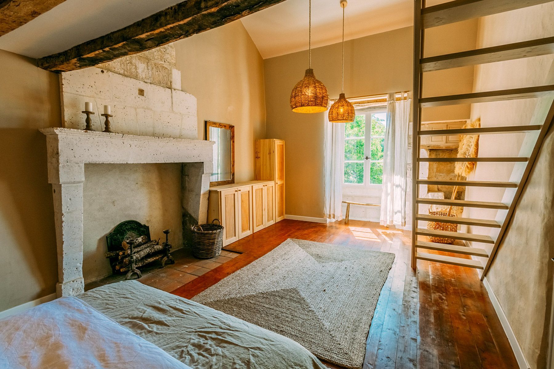 A rustic room with a fireplace, wooden beams, a loft bed, and a hanging light fixture.