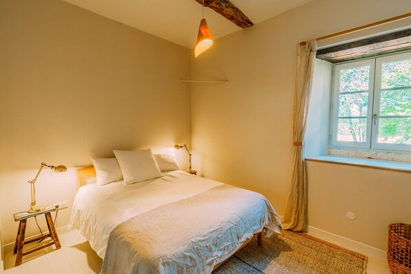 A bedroom with a bed, bedside lamps, a window with curtains, and a rustic ceiling beam.