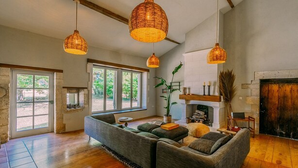 Een ruime woonkamer met een grote hoekbank, een open haard en drie hangende rieten lampen.