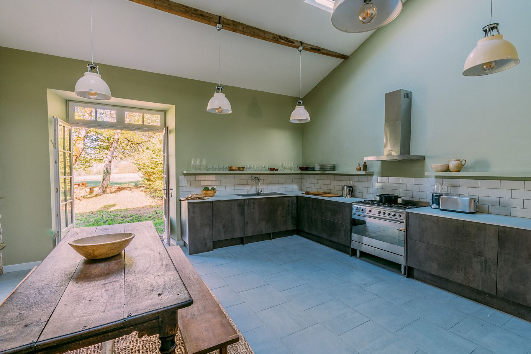 Una cocina con una mesa de madera, estufa y lámparas colgantes.