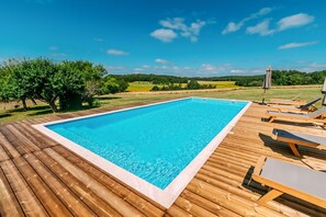 Una piscina rectangular con un deck de madera alrededor, equipada con sillas de descanso y una sombrilla.