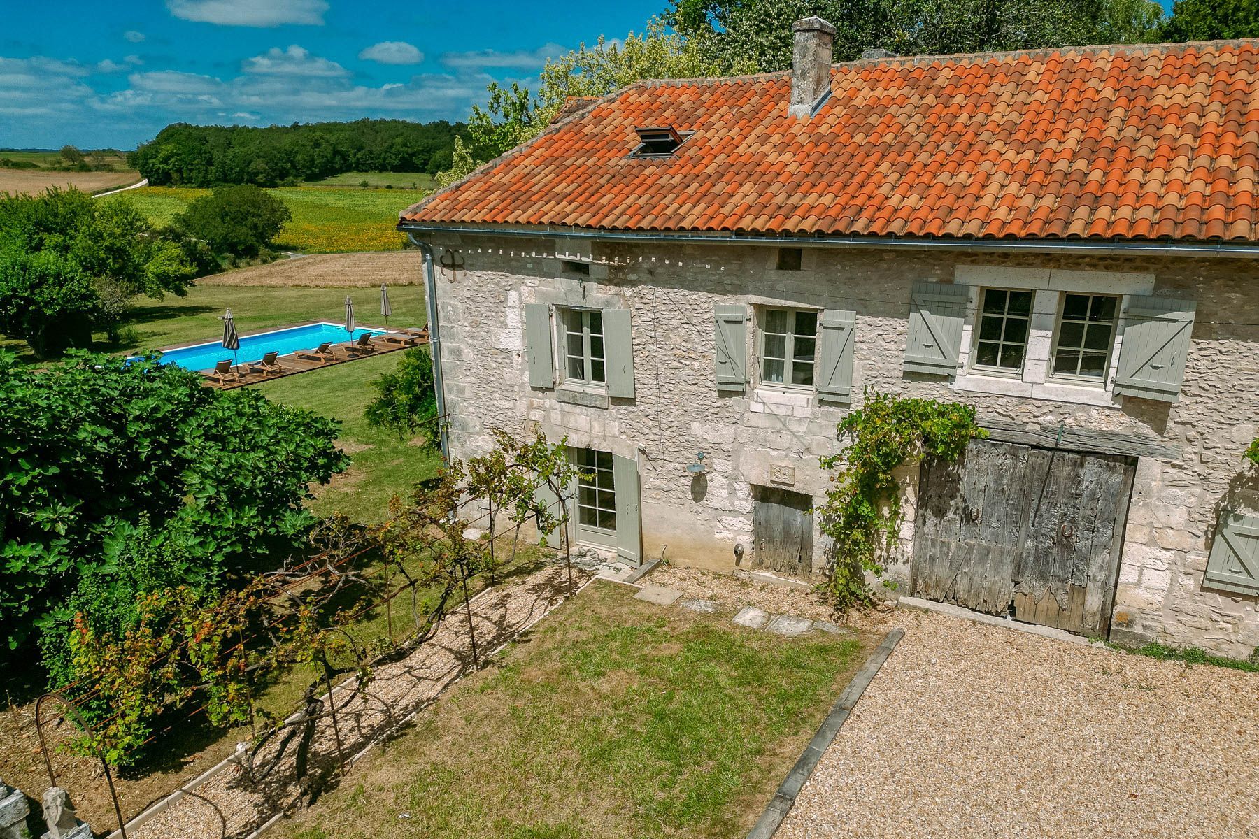 Une maison en pierre avec un toit recouvert de tuiles rouges, une piscine et un vignoble.