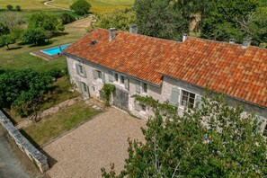 A stone building with a red-tiled roof, a swimming pool, and a gravel driveway.