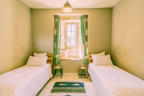 A room with two beds, a window with curtains, a small table, and a lamp.