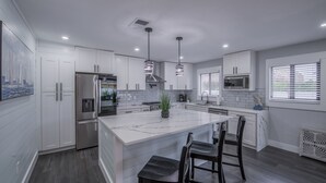Una cocina moderna con armarios blancos, un refrigerador de acero inoxidable, una isla de mármol e iluminación colgante.