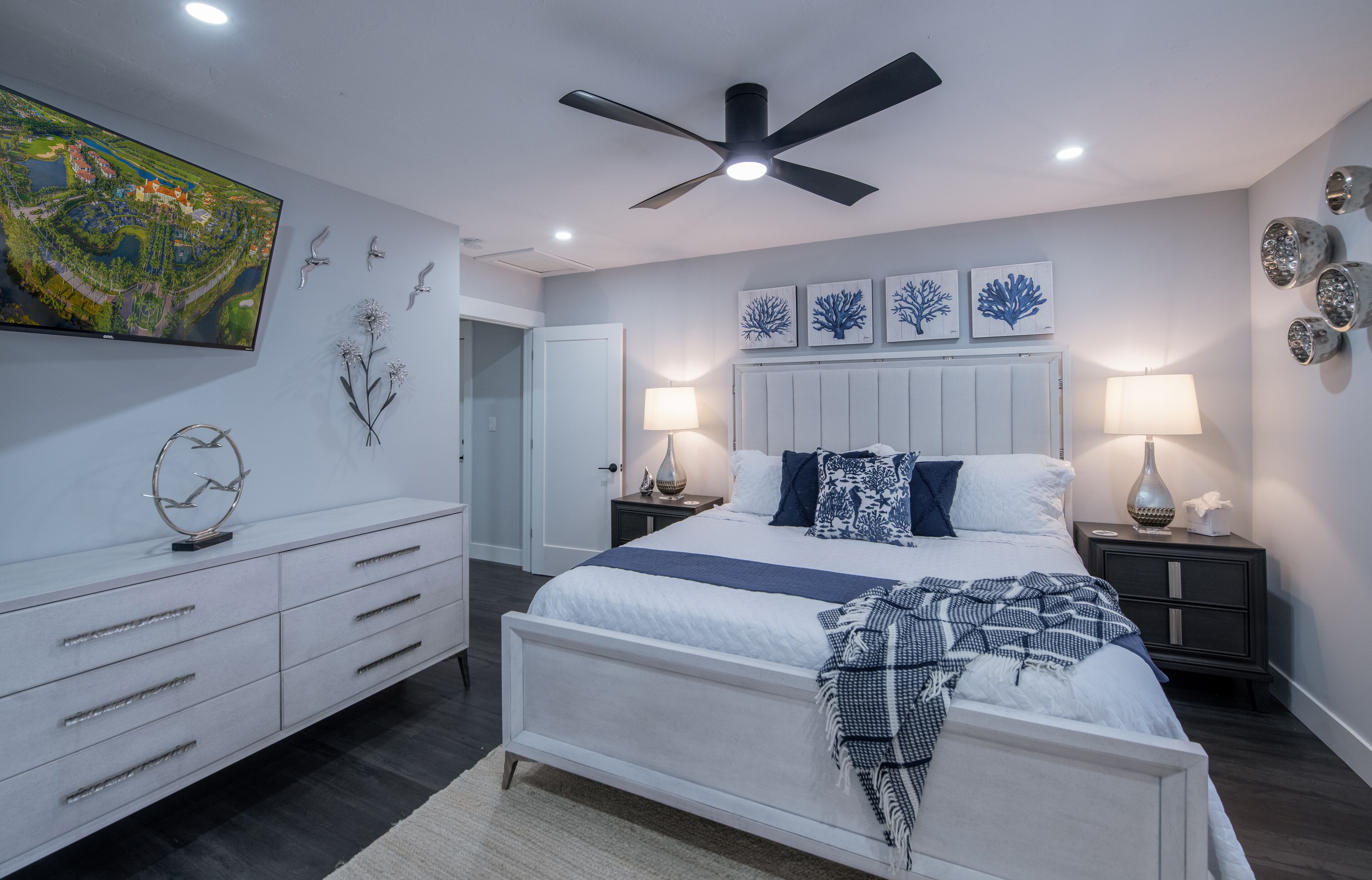 Une chambre moderne avec un grand lit, un ventilateur de plafond, une télévision et des œuvres d’art décoratives au mur.