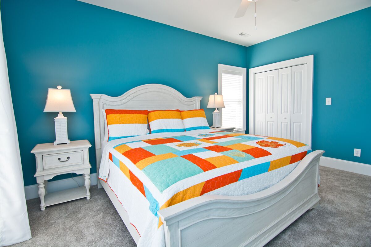 A bedroom with a white bed, teal walls, and a colorful quilt.