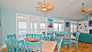 A dining area with turquoise chairs and a wooden table, a teal sofa, and a ceiling fan. - Pa's Place, Almost Oceanfront House in Emerald Isle, NC! (Emerald Isle)