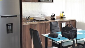 A compact kitchenette with a refrigerator, a water dispenser, a kettle, and a coffee maker. There is a dining table with two chairs and a black bag on it. - Suite moderna 301. La Mejor Ubicación

 (Quito)