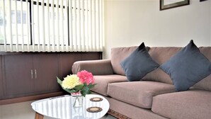A living room with a beige sofa, two dark pillows, a glass coffee table with wooden legs, and a vase with flowers. - Suite moderna 301. La Mejor Ubicación

 (Quito)