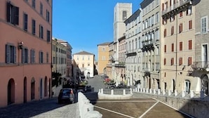 Una strada acciottolata fiancheggiata da edifici storici, una fontana al centro e un cielo azzurro limpido.