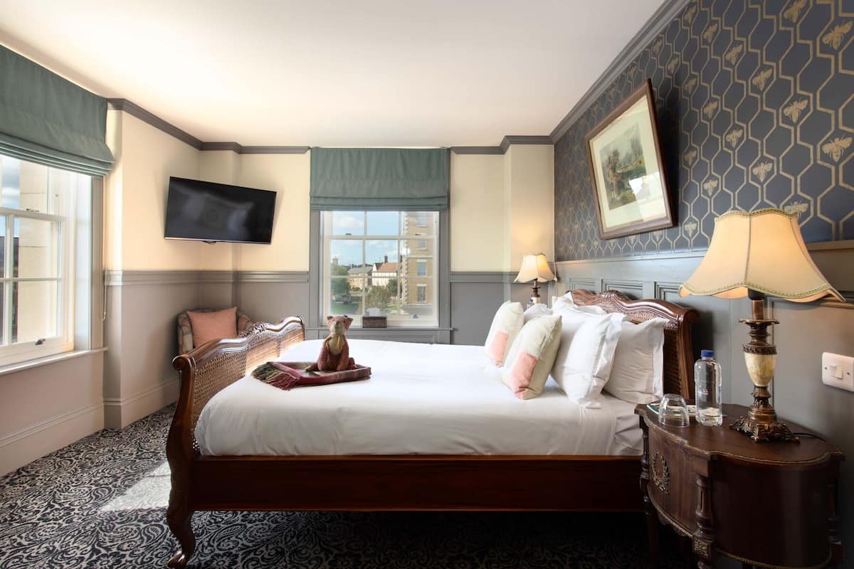 A neatly made bed with pillows and a small table with a lamp and a bottle.