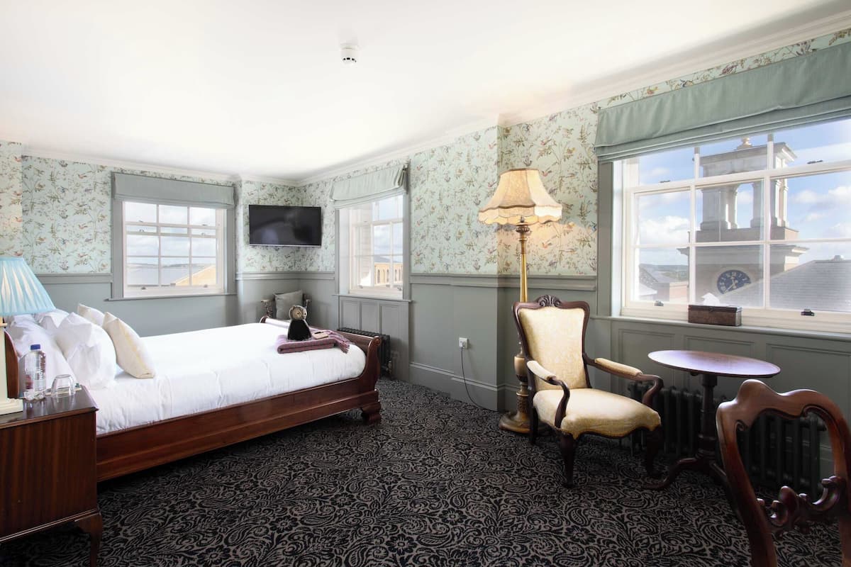A hotel room with a bed, a chair, a table, a lamp, and a TV.