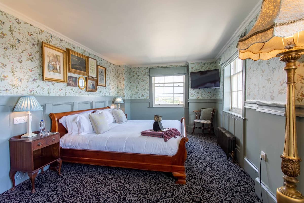 A bedroom with a wooden bed, a nightstand, a lamp, a dresser, a mirror, and a window with a view.