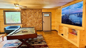 Um quarto aconchegante com mesa de bilhar, uma grande janela com vista para a cidade e uma parede de madeira com toras.