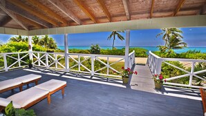 Un espace extérieur abrité, doté de bancs en bois et de plantes en pot, offrant une vue sur la plage et l’océan.