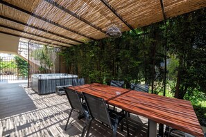 An outdoor dining area with a wooden table and chairs, a hot tub, and a bamboo ceiling.