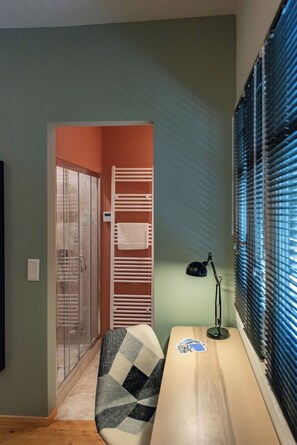 A room with a wooden desk, a chair, a lamp, a towel rack, and a glass door leading to another room. - Country Home - Kalamata Mediterranean Suites & Villas
 (Kalamata)