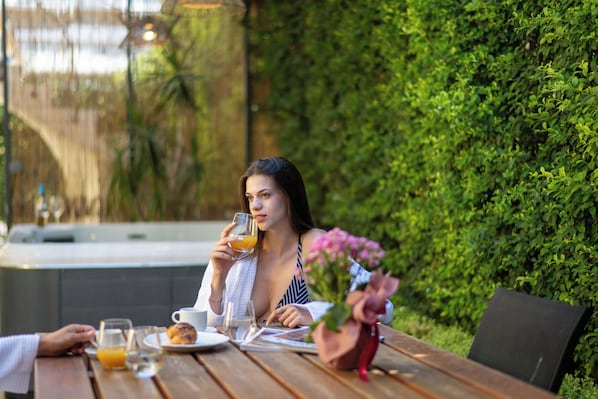 A woman sitting at an outdoor wooden table with a glass of orange juice, a cup, and a plate with food.